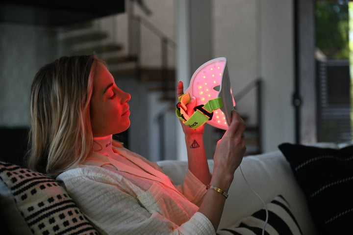 Woman relaxing at home while using the Glotech™ Mask Pro red light therapy face mask, a non-invasive treatment to calm rosacea, reduce redness, and improve skin health.