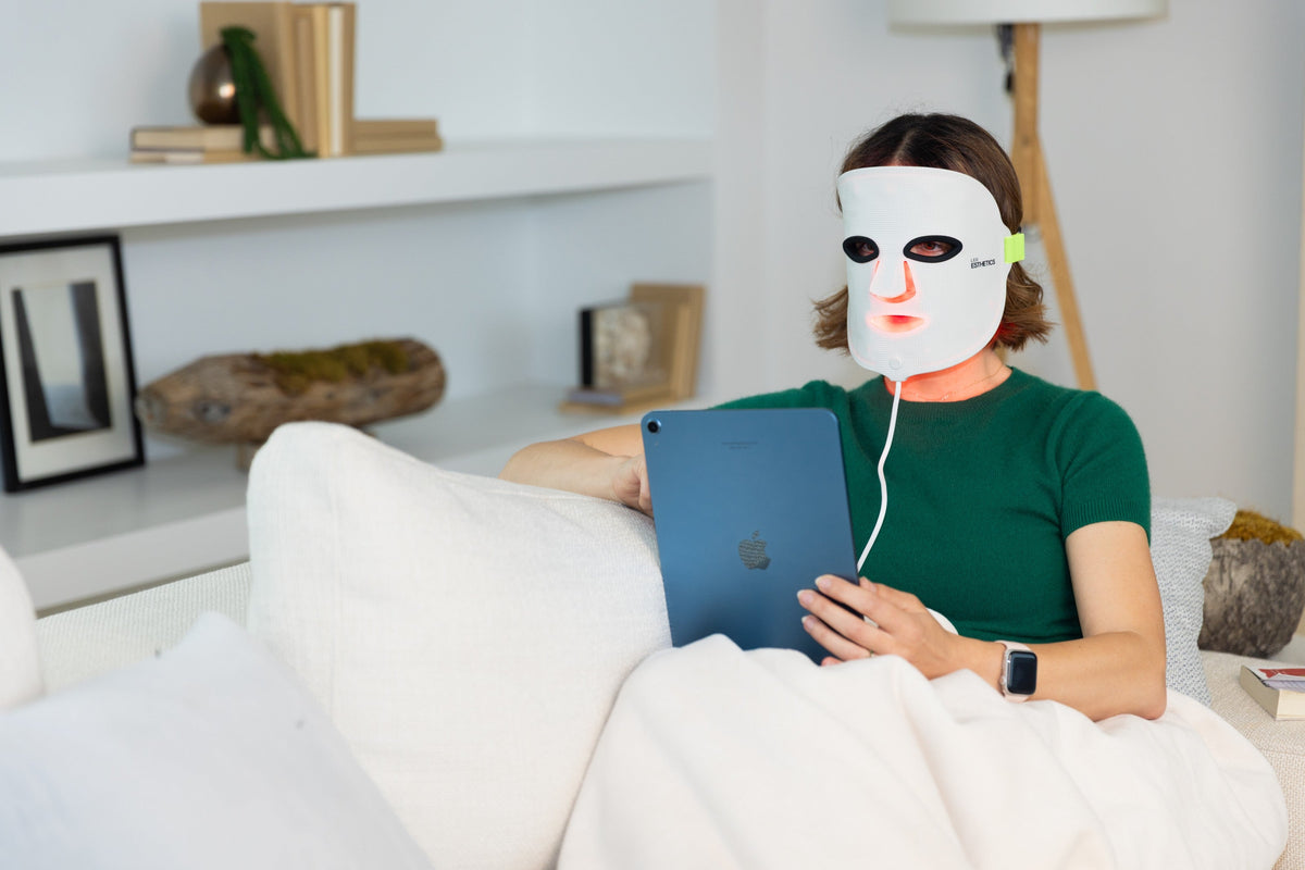Woman relaxing on a couch while wearing the GloTech™ LED face mask, enjoying red light therapy for skin rejuvenation and acne treatment at home.