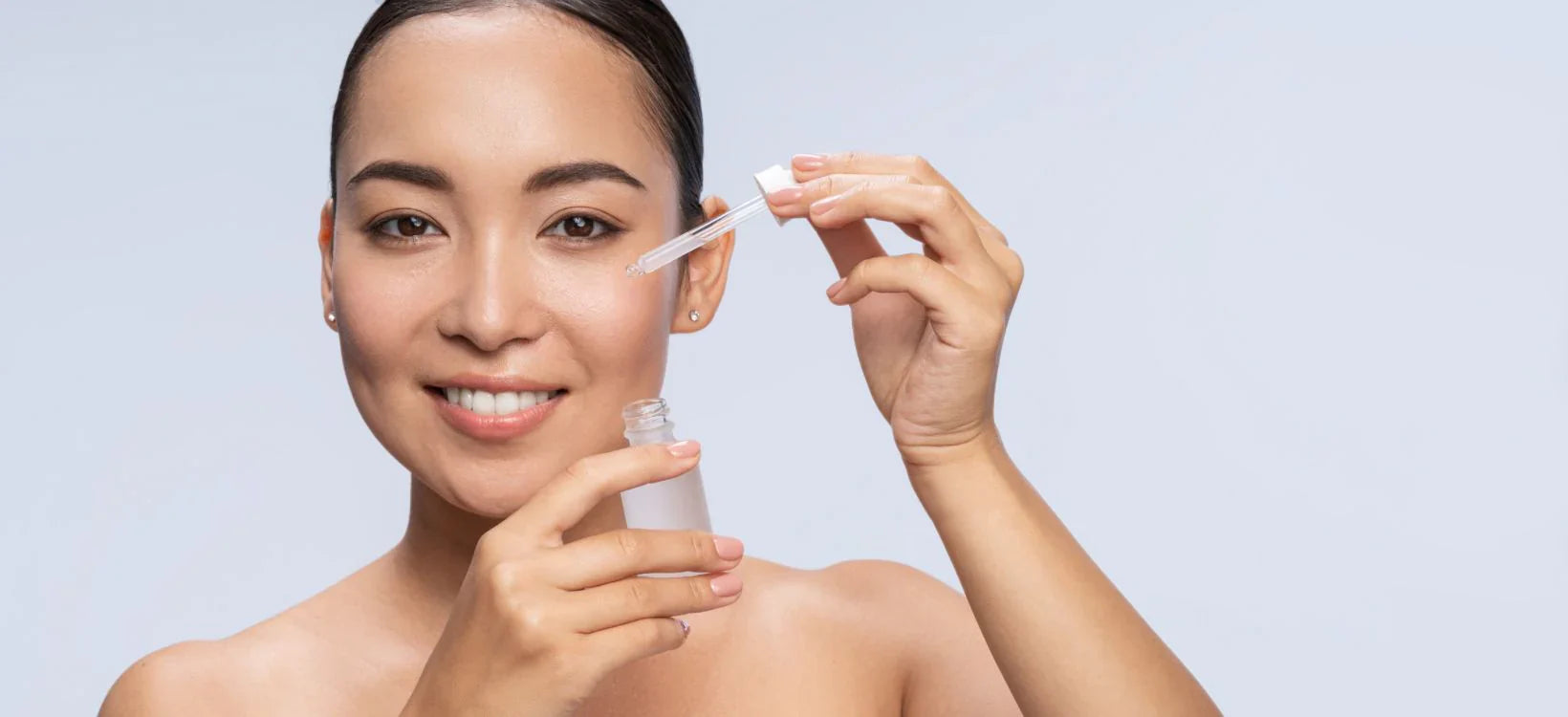 Woman applying serum with a dropper for skincare routine, smiling with a radiant complexion.