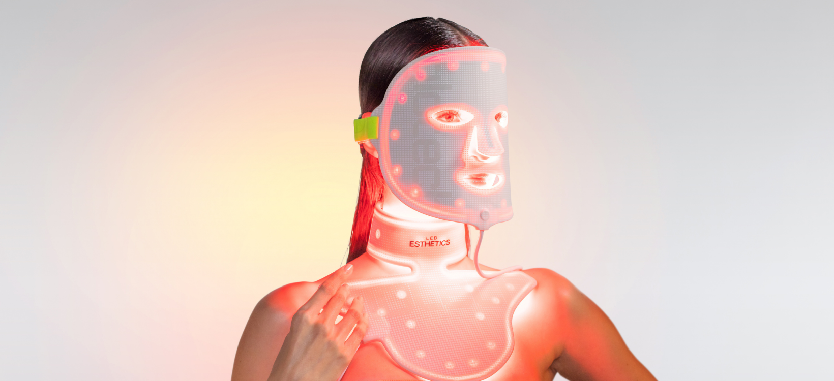 Person wearing red LED light therapy face and neck mask for skin treatment.