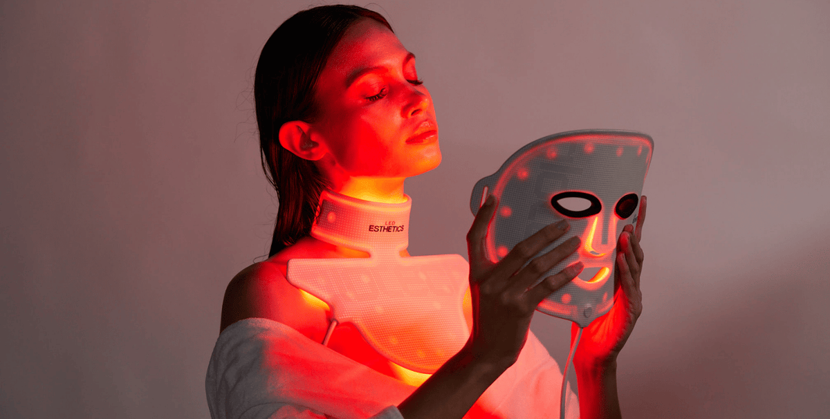 Woman using red LED light therapy mask and neck device to help fade post-acne marks and support skin repair.