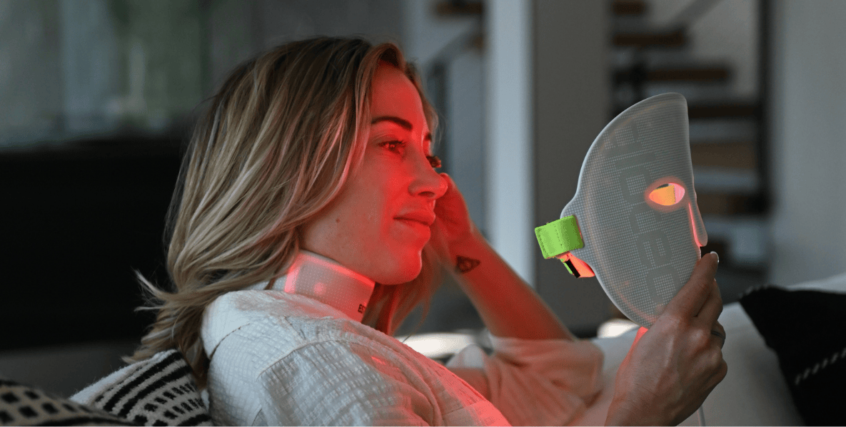 Woman holding the Glotech Mask Pro red light therapy device near her face at home as part of an adult acne skincare routine.