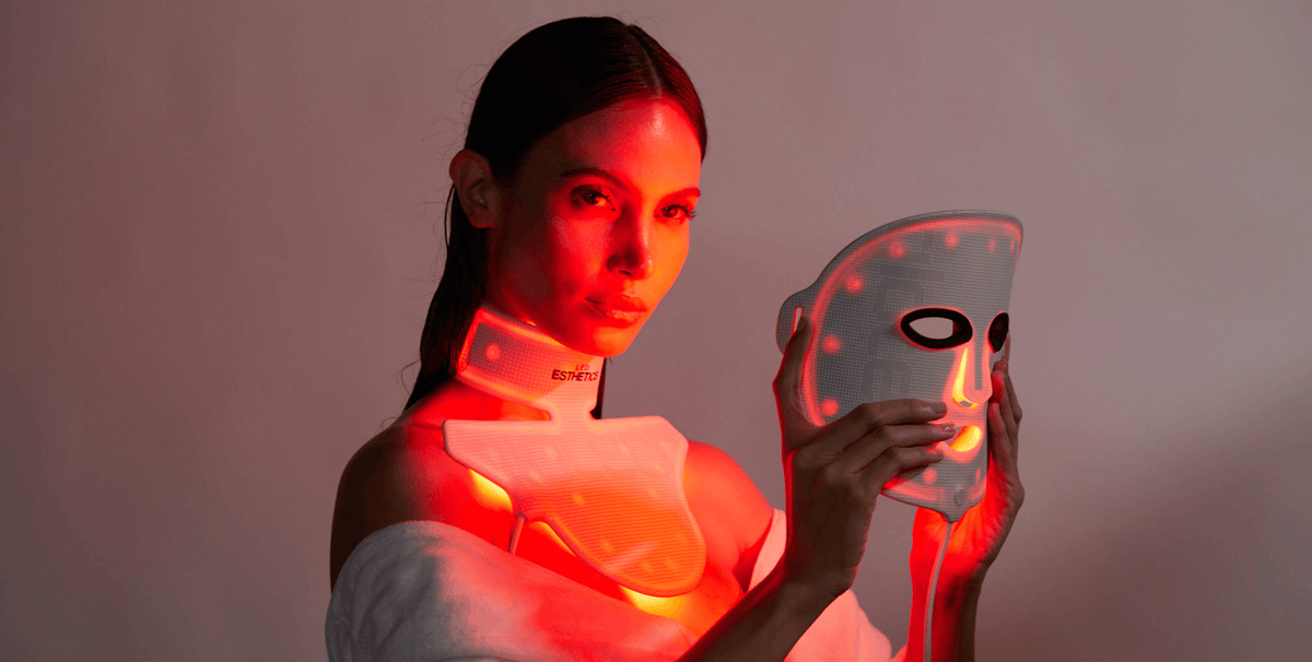 Red light therapy mask and neck and chest collar being used by a woman, demonstrating at-home LED treatment for autoimmune skin conditions.