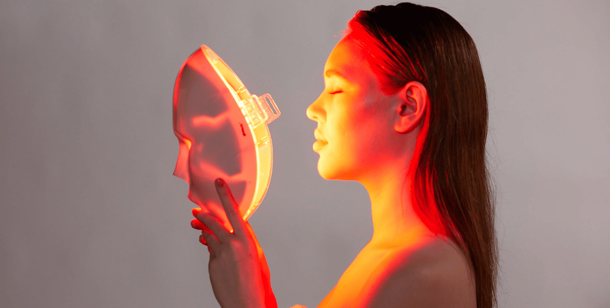 Woman holding the Glotech Mask Lite emitting red light therapy close to her face for rosacea treatment at home.